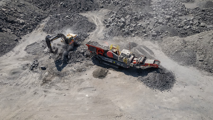 Mobile crushing plant running under lights beside a growing product stockpile.